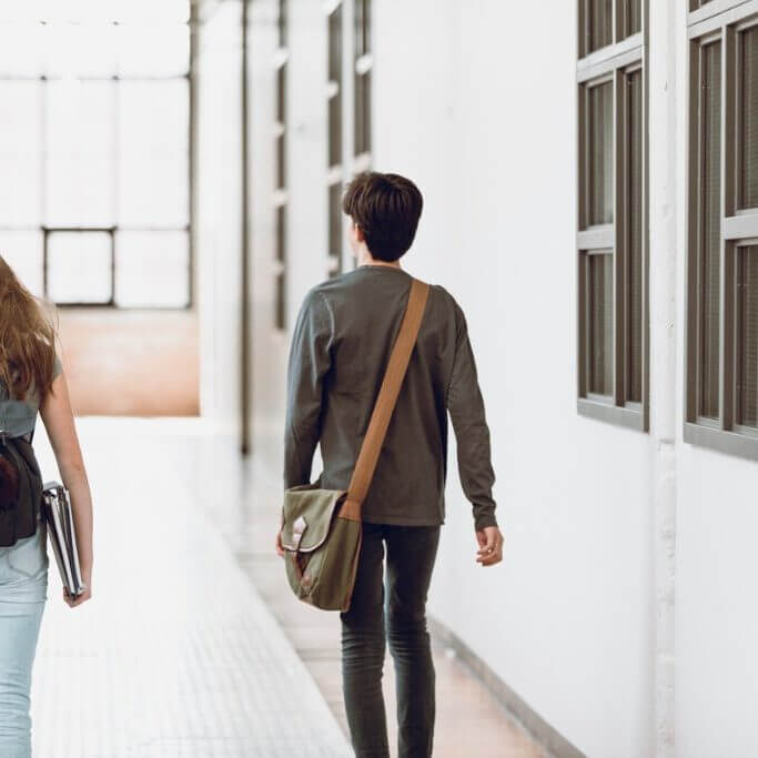 two-teenagers-walking-in-the-corridor-at-school-rear-view-one-boy-and-picture-id937049066-square